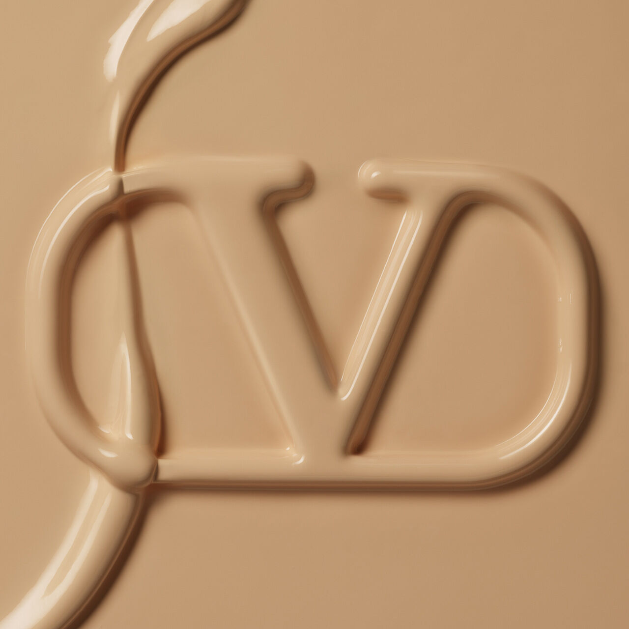 A close-up image of a smooth, beige liquid that has the letters "CD" artistically formed within it, resembling a cosmetic or skincare product.