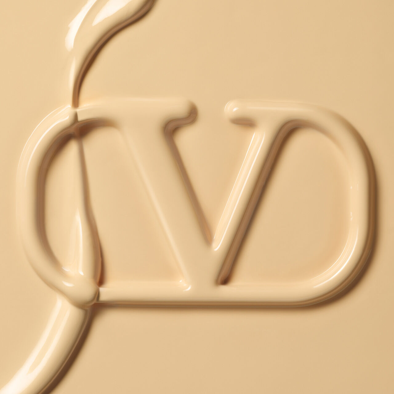 Close-up of a creamy, beige substance forming the letters "VD" in a smooth, flowing style.