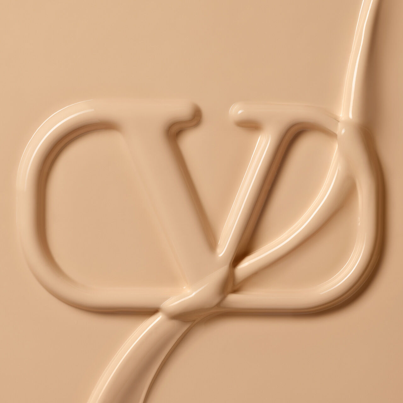 A close-up of creamy beige product with an embossed letter "Y" and a fluid line swirling around it, creating a textured appearance.