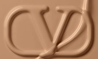 Close-up of a smooth, beige creamy texture with a stylized logo embossed into it, resembling the letters "CD."