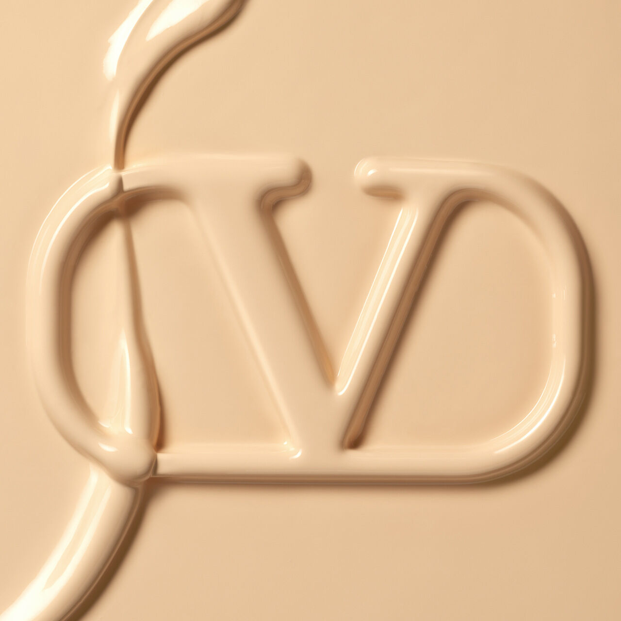 Close-up of a creamy, light beige substance forming the initials "CD" in a stylized, fluid design.