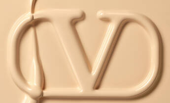 Close-up of a creamy, light beige substance forming the initials "CD" in a stylized, fluid design.
