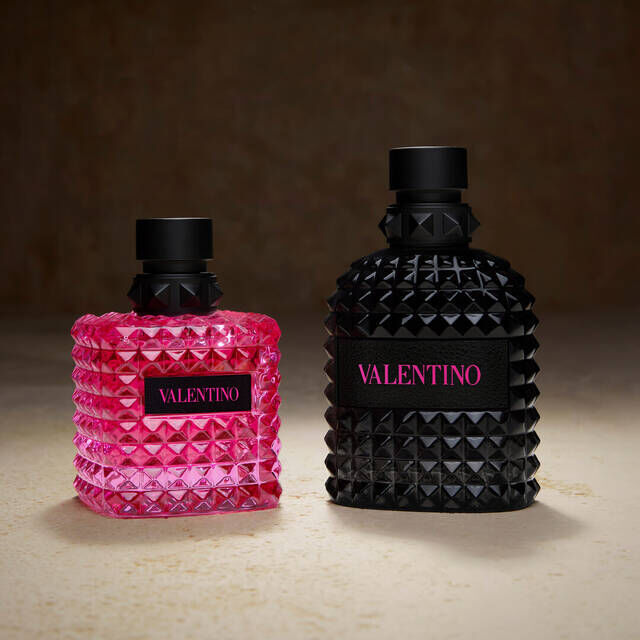 Two Valentino perfume bottles, one pink and one black, featuring a textured, pyramid-studded design on a neutral background.