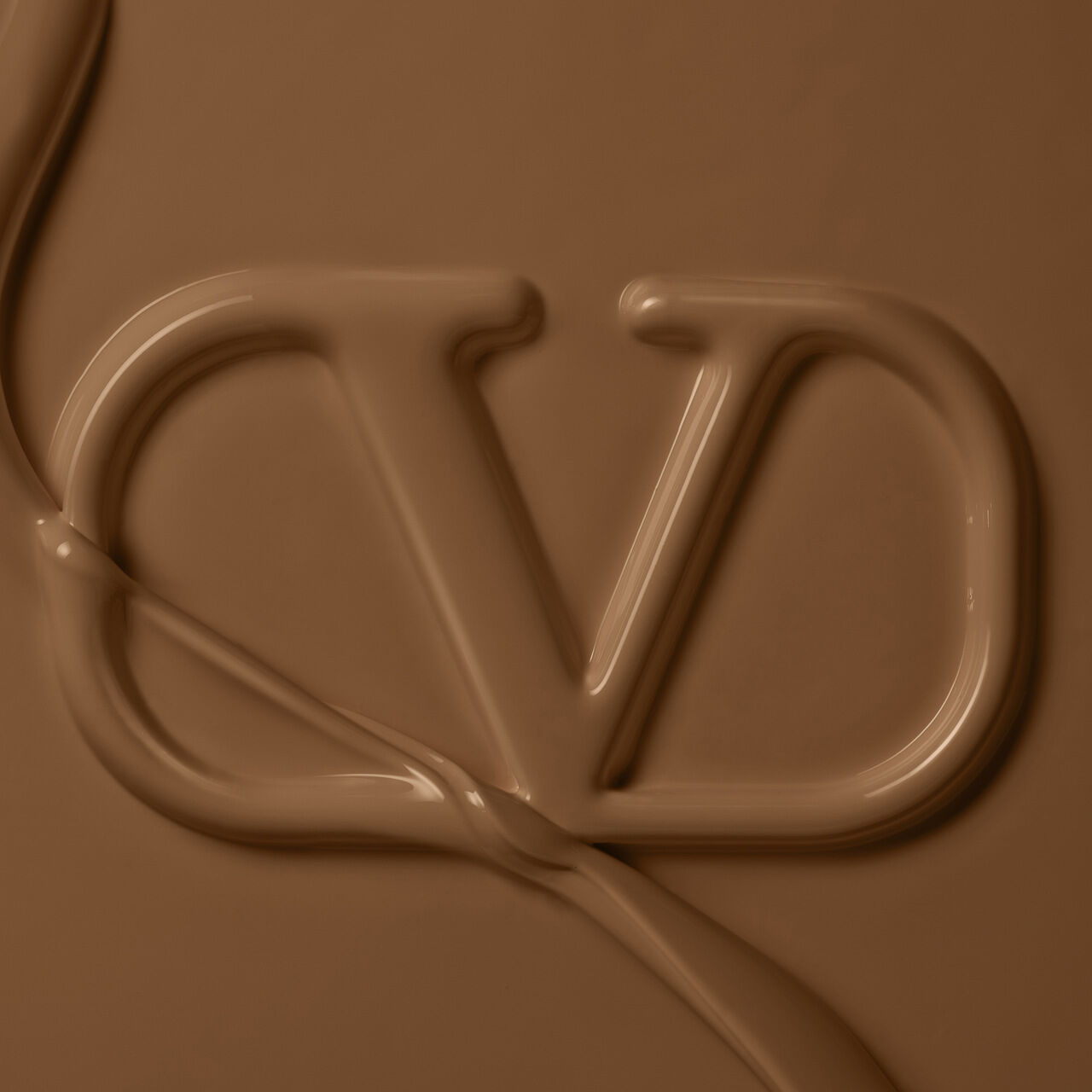 A close-up of a creamy, chocolate-colored surface featuring an elegant, stylized "VD" logo created with smooth, flowing texture.