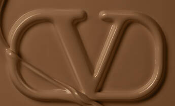 A close-up of a creamy, chocolate-colored surface featuring an elegant, stylized "VD" logo created with smooth, flowing texture.