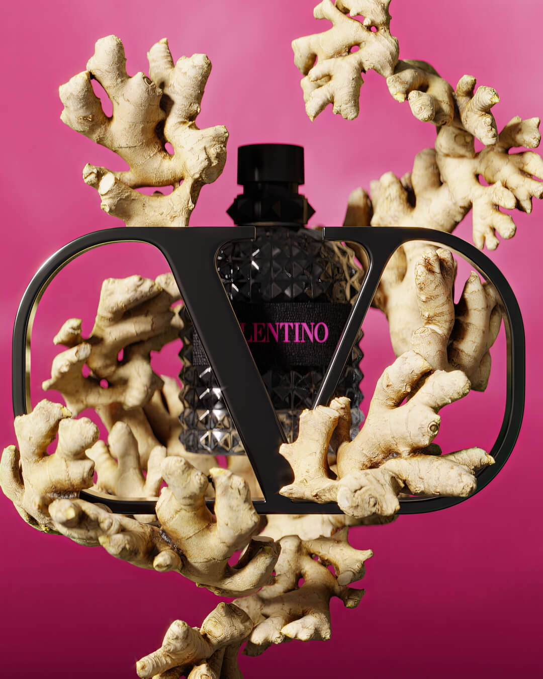 A stylish black bottle of Valentino perfume is surrounded by coral-like structures against a bright pink background. The bottle features a textured design and a prominent "V" logo.