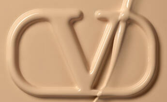 Close-up view of a smooth, beige cream or foundation featuring a prominent embossed logo that reads "CD."