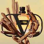 A stylish perfume bottle with a geometric design is surrounded by twisting branches, creating a modern and artistic display. The bottle features the brand name "Valentino" prominently on its label.