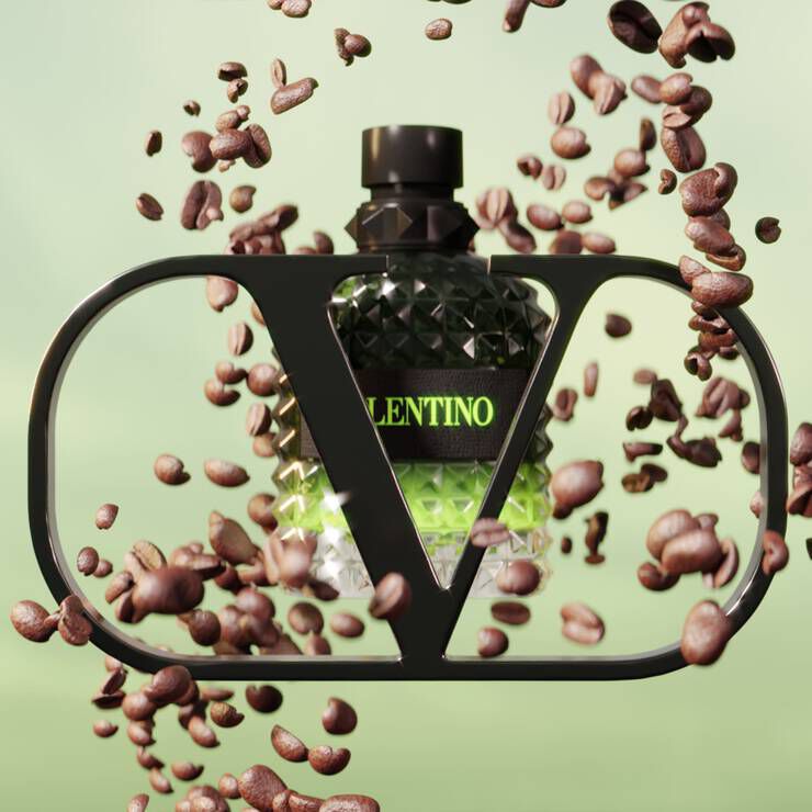 A stylized perfume bottle with a geometric design is framed by a black outline. Surrounding the bottle are scattered coffee beans, creating a dynamic, energetic feel against a soft green background. The bottle features bold text that reads "VALENTINO."