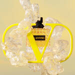 A perfume bottle with a diamond-patterned design sits behind a large yellow "V" and "D" logo, surrounded by translucent, bubbly elements, all set against a soft yellow background.