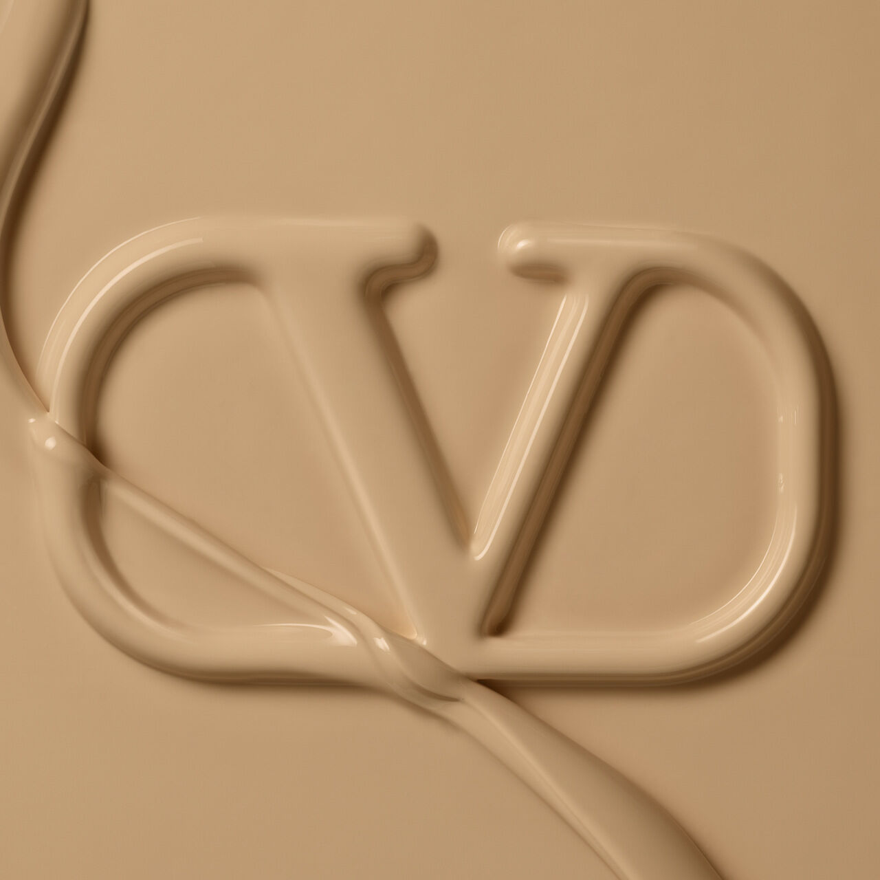 A close-up of a creamy beige surface featuring the stylized letters "VD" formed by a smooth, flowing substance.