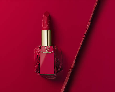 A striking red lipstick in a stylish gold and glass container, placed on a matching red background with a clean, modern aesthetic.