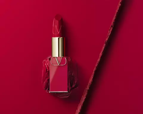 A striking red lipstick in a stylish gold and glass container, placed on a matching red background with a clean, modern aesthetic.