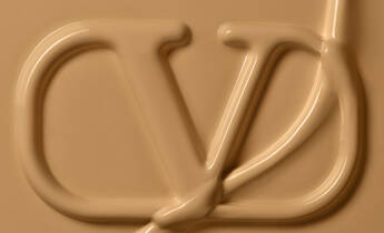 An abstract image featuring a stylized logo or emblem in a smooth, beige texture. The logo appears to be created from a thick, flowing substance, giving it a three-dimensional look.