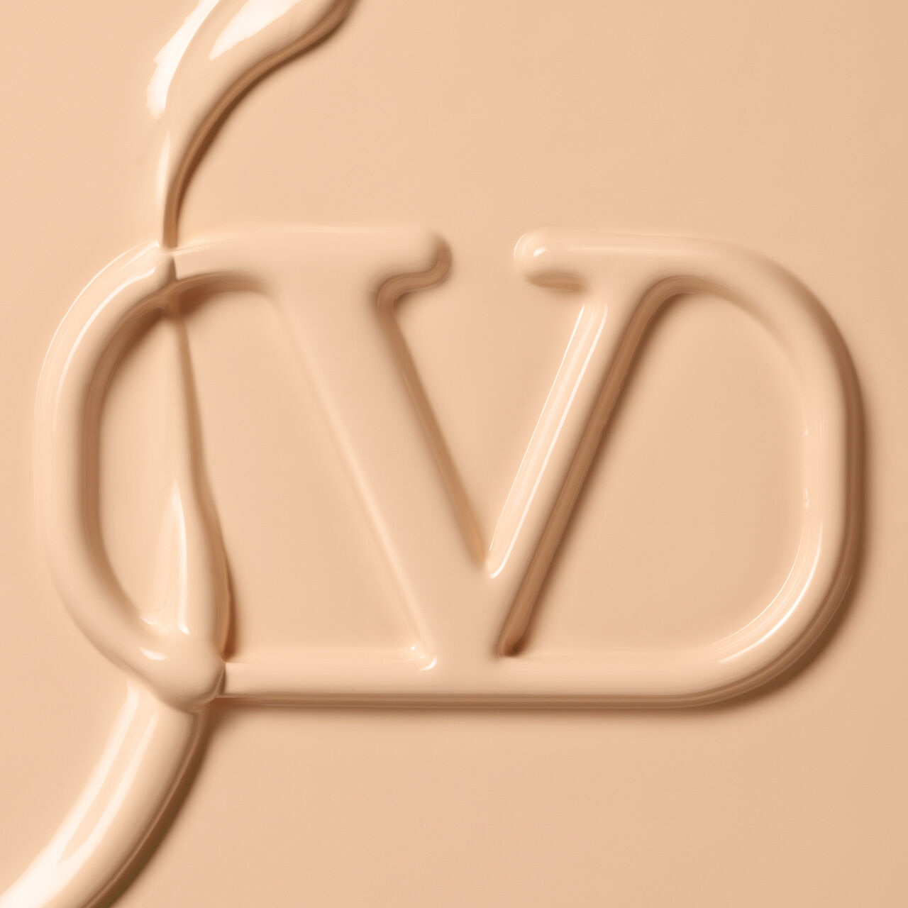 Close-up of a creamy, beige liquid forming the letters "J" and "D" against a smooth surface.