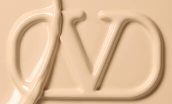 A close-up image of a creamy, beige substance shaped into the letters "D" and "V" against a smooth, neutral background.