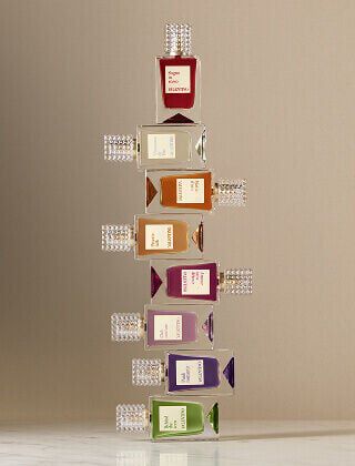 A row of eight Valentino perfume bottles in different colors, each with a textured transparent cap, arranged on a light surface against a beige background.