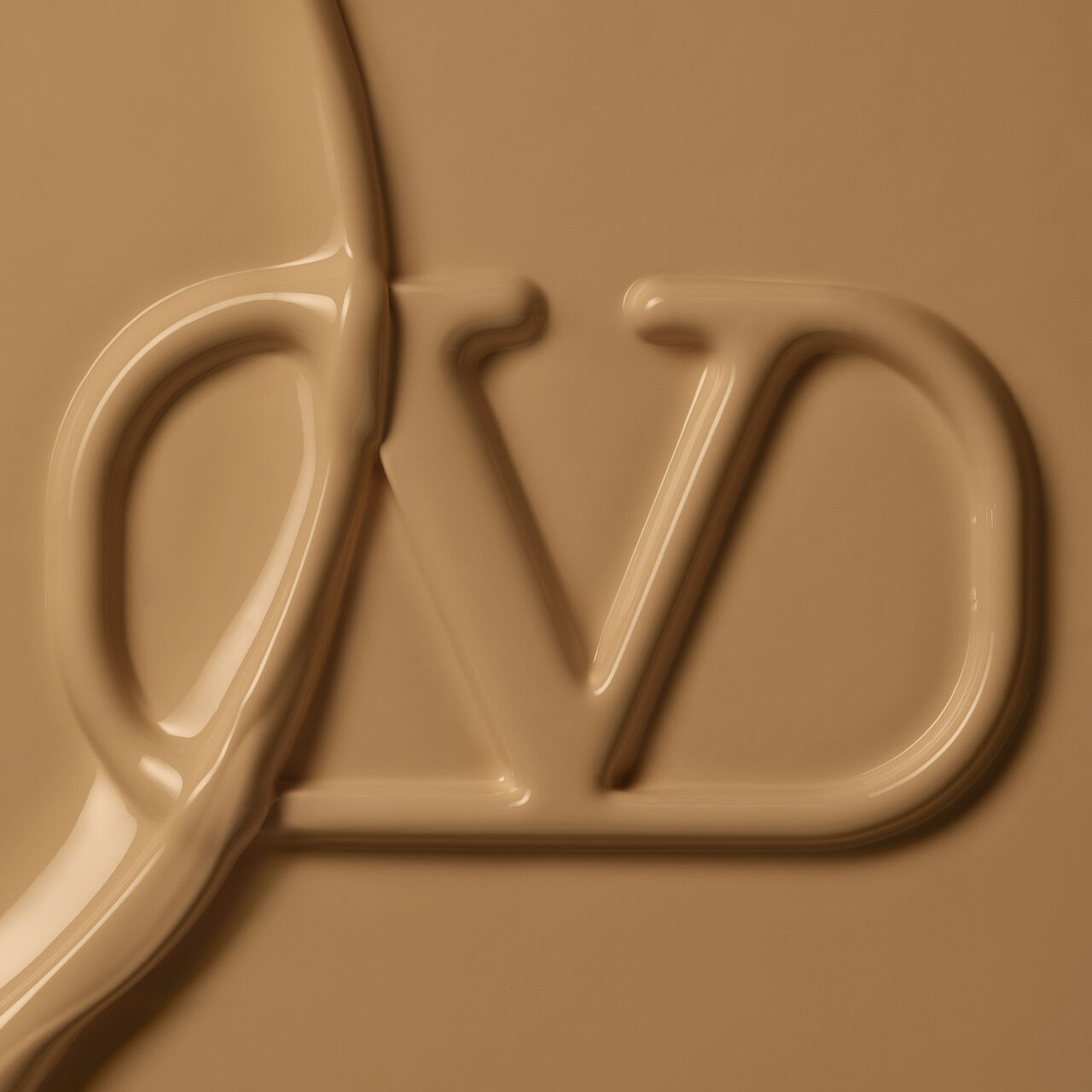 Close-up of a smooth, creamy substance with a stylized "VD" logo embossed in it, set against a warm beige background.