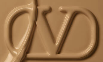 Close-up of smooth, caramel-colored liquid with a stylized "DV" logo partially visible.